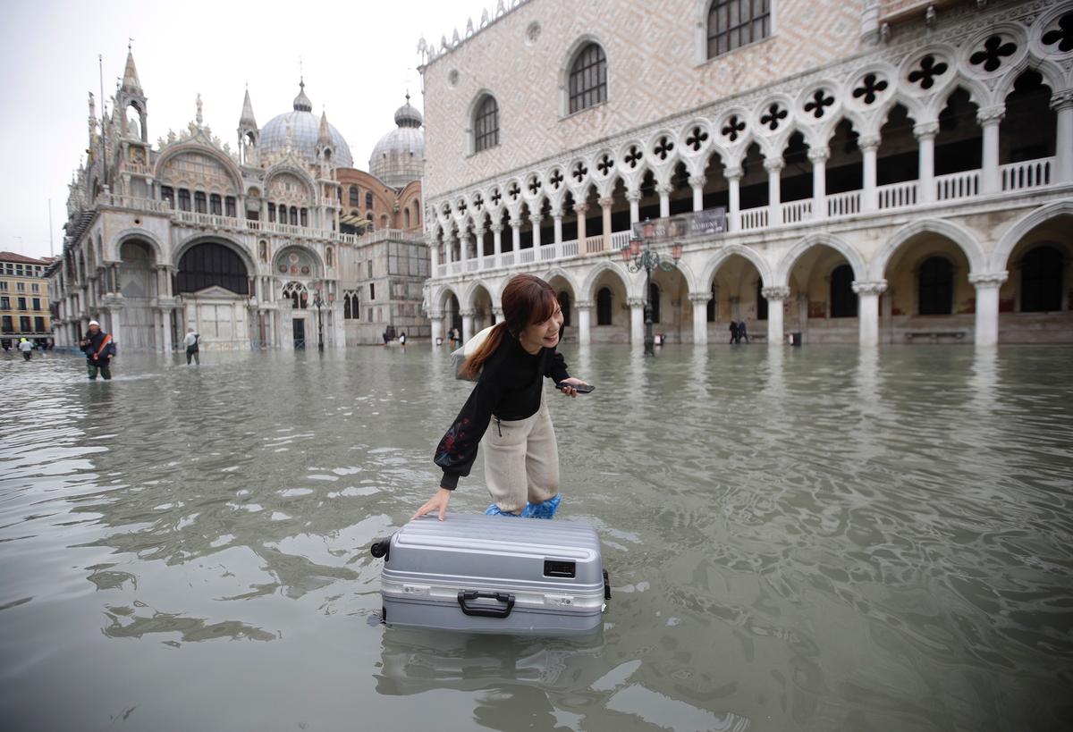 A tourist pushes her floating luggage in a flooded St. Mark's Square, in Venice, on Nov. 13, 2019. (AP Photo/Luca Bruno)