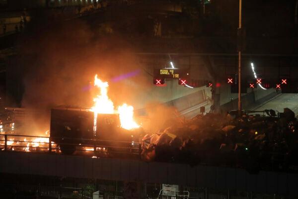 An armored police vehicle catches fire after being hit by molotov cocktails thrown by protestors, at right, on a bridge over a highway leading to the Cross Harbor Tunnel in Hong Kong, on Nov. 17, 2019. (AP Photo/Kin Cheung)