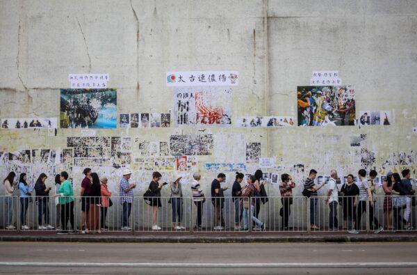 People queue to cast their vote in front of a "Lennon Wall" adorned with tattered posters in support of the ongoing protests, during the district council elections in Tai Koo in Hong Kong on Nov. 24, 2019. (Vivek Prakash/AFP via Getty Images)