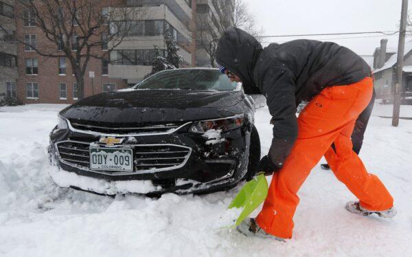 Erik Randa helps dig out a stuck Chevrolet Malibu being used by a ride-sharing service driver out of an intersection at 2nd Ave. and Pearl St. as a storm packing snow and high winds sweeps in over the region on Nov. 26, 2019, in Denver. (David Zalubowski/AP Photo)