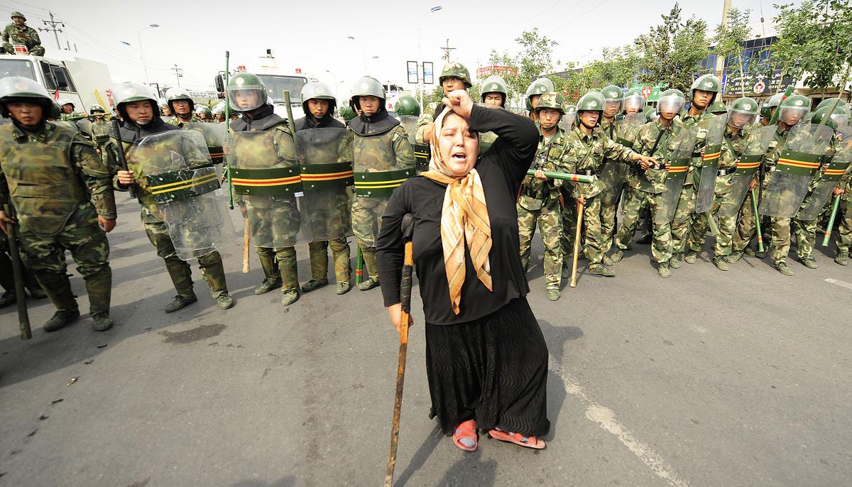 Chinese riot police watch a Muslim ethnic Uyghur woman protest in Urumqi in China's far west Xinjiang Province. (©Getty Images | <a href="https://www.gettyimages.com/detail/news-photo/chinese-riot-police-watch-a-muslim-ethnic-uighur-woman-news-photo/111974525?adppopup=true">PETER PARKS</a>)