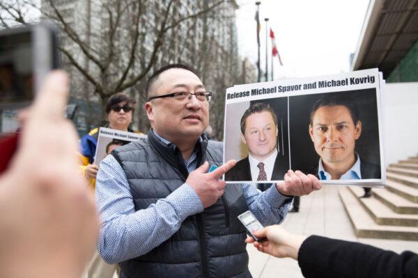 Louis Huang of Vancouver Freedom and Democracy for China holds photos of Canadians Michael Spavor and Michael Kovrig, who are being detained by China, outside British Columbia Supreme Court, in Vancouver, on March 6, 2019, as Huawei Chief Financial Officer Meng Wanzhou appears in court. (Jason Redmond/AFP via Getty Images)