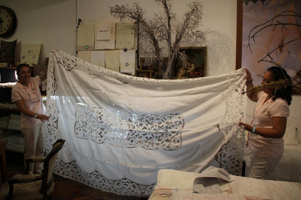 Marcia Gomes (L) shows a tablecloth priced at $4,000 at Bordados da Madeira. (Wibke Carter)