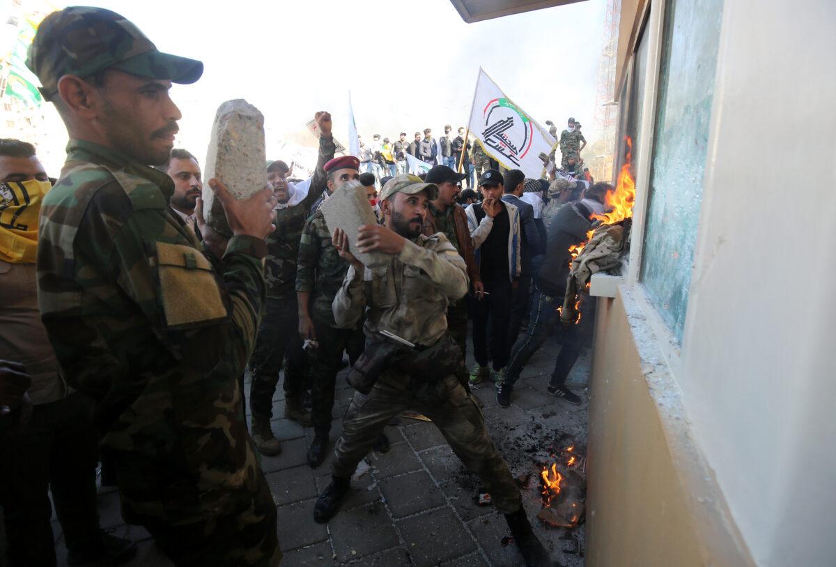 Members the Hashed al-Shaabi, a terrorist group trained and armed by Iran, smash the bullet-proof glass of the U.S. embassy's windows in Baghdad with blocks of cement after breaching the outer wall of the diplomatic mission on Dec. 31, 2019. (Ahmad Al-Rubaye/AFP via Getty Images)