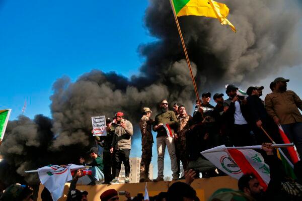 Attackers waving the Kataib Hezbollah terrorist group flag burn property in front of the U.S. Embassy compound, in Baghdad, Iraq, on Dec. 31, 2019. (Khalid Mohammed/AP)