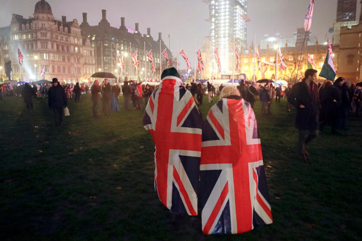 People draped in UK flags walk across Parliament Square during rainfall in London, Friday, Jan. 31, 2020. (Kirsty Wigglesworth/AP Photo)