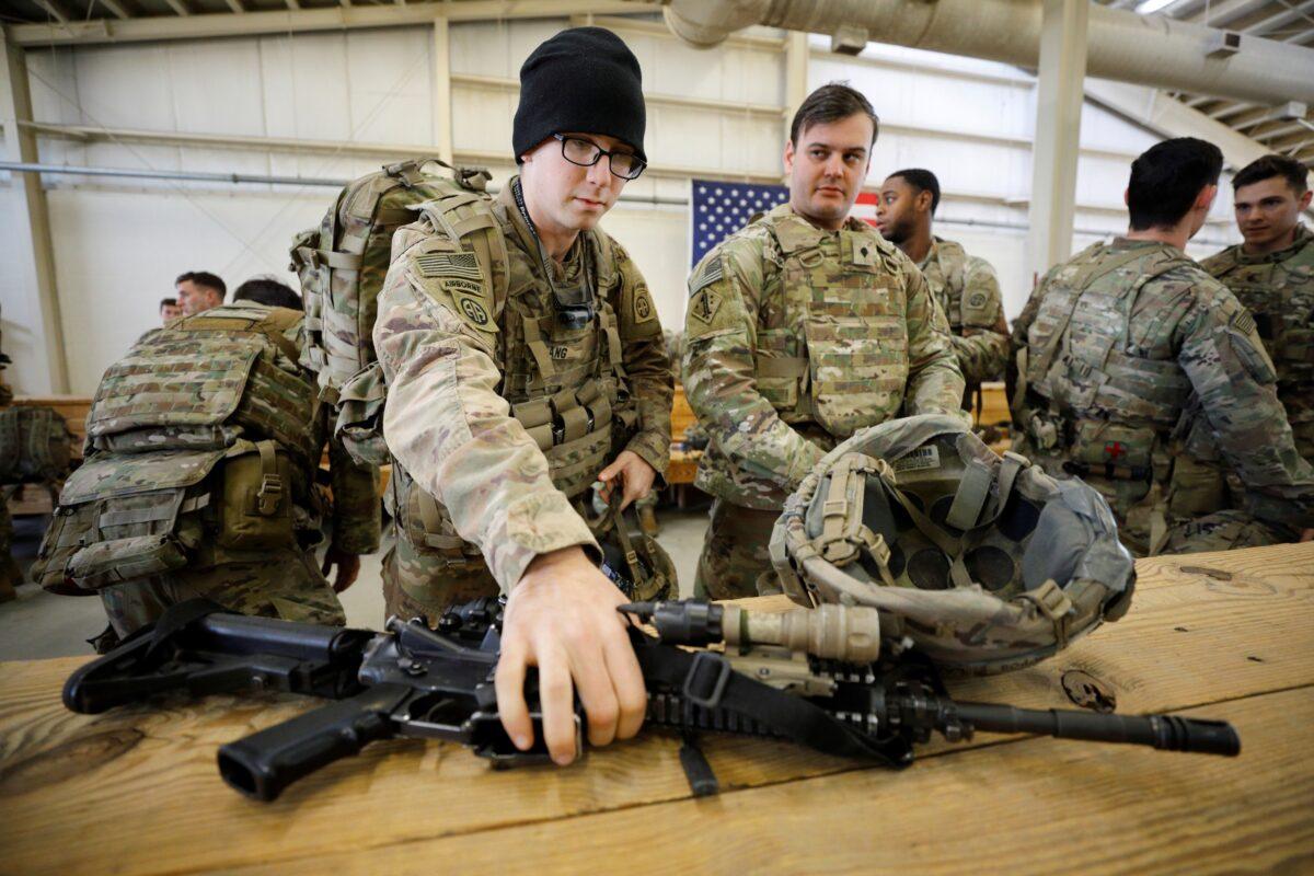 A U.S. Army paratrooper of an immediate reaction force from the 2nd Battalion, 504th Parachute Infantry Regiment, 1st Brigade Combat Team, 82nd Airborne Division, reaches for his weapon shortly before boarding a C-17 transport aircraft leaving Fort Bragg, North Carolina on Jan. 1, 2020. (Jonathan Drake/Reuters)