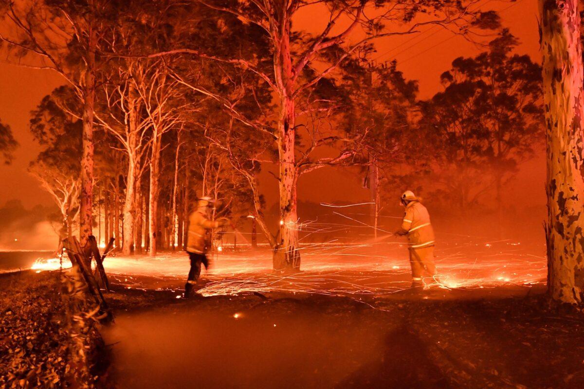 This timed-exposure image shows firefighters hosing down trees as they battle against bushfires around the town of Nowra in the Australian state of New South Wales on Dec. 31, 2019. (Saeed Khan/AFP via Getty Images)