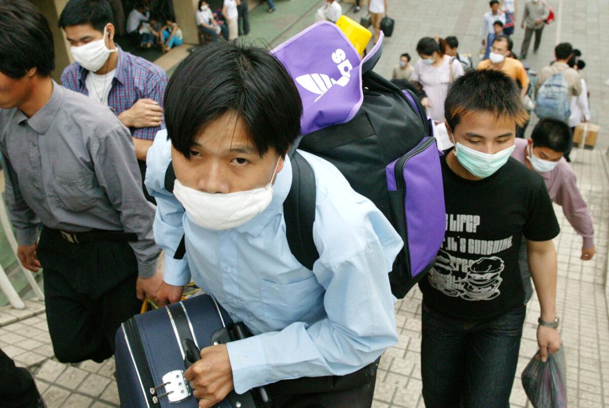 Migrant workers wearing protective face masks make their way to the train station as they leave the city over worries about SARS in Guangzhou, the capital of Guangdong province, China, on May 2, 2003. (Christian Keenan/Getty Images)