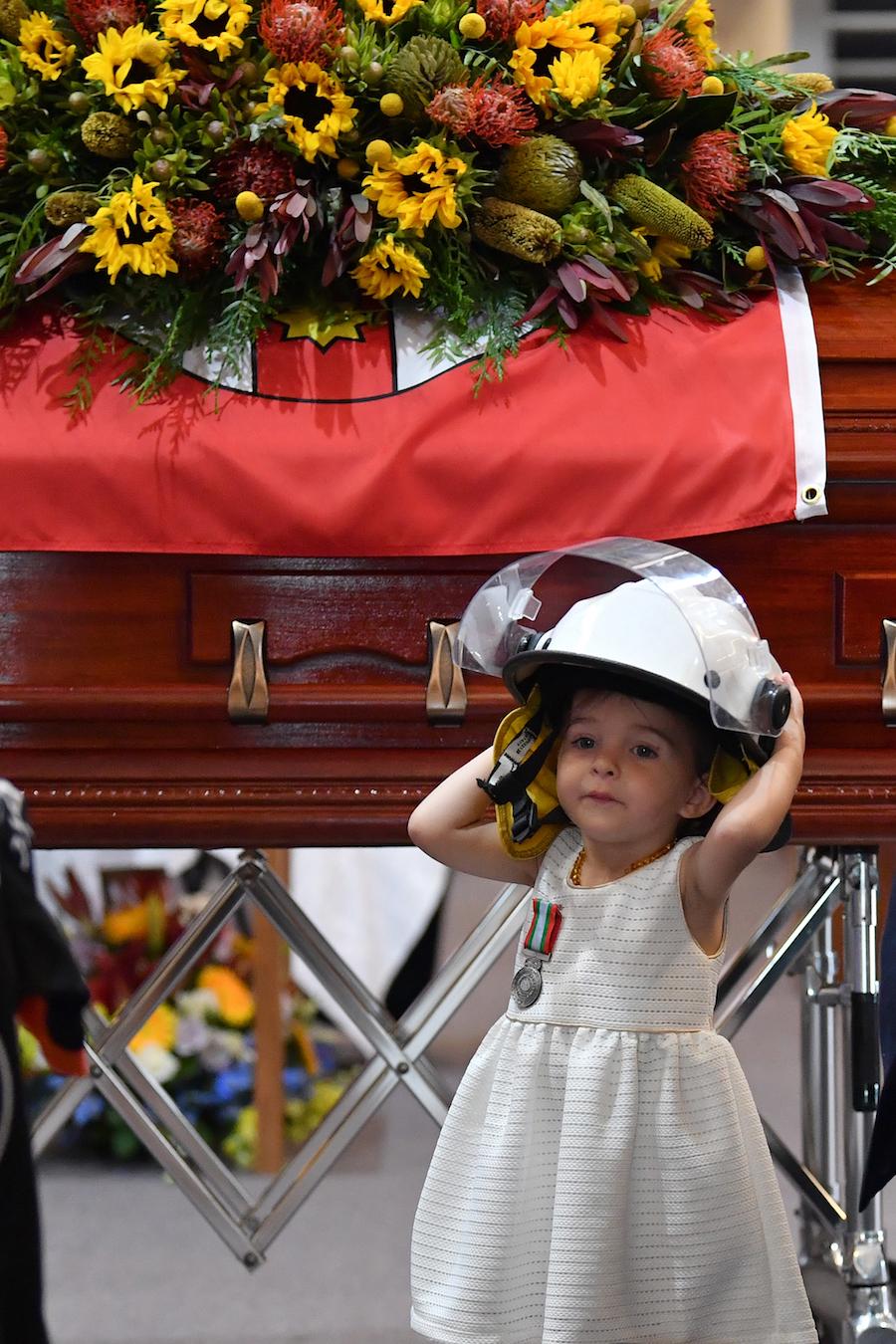 Charlotte O'Dwyer, pinned with a medal for bravery and her father's helmet, stands next to Geoffrey O'Dwyer's coffin at his funeral service in Sydney, Australia. (©Getty Images | <a href="https://www.gettyimages.com/detail/news-photo/charlotte-odwyer-the-young-daughter-of-rural-fire-service-news-photo/1192337551?adppopup=true">Dean Lewins-Pool</a>)