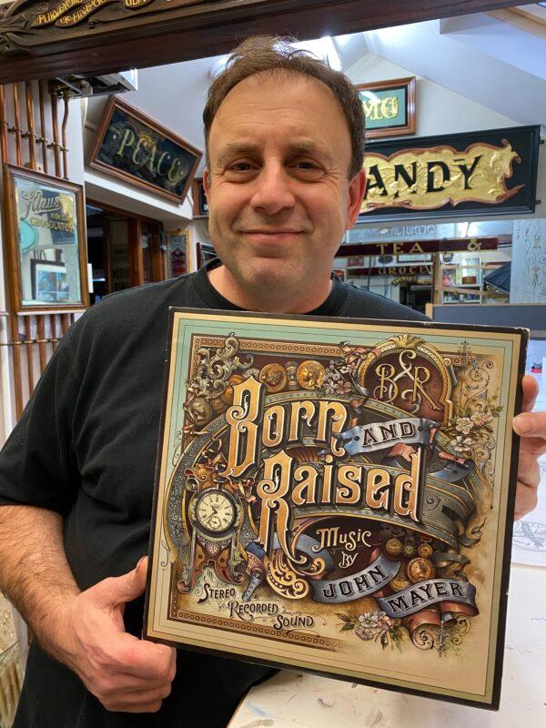 David Adrian Smith in his workshop in Torquay, Devon, UK, on Jan. 13, 2020. Smith holds a copy of John Mayer's album "Born and Raised," which he designed in 2012. (Hannah Smith)