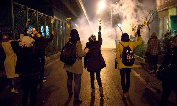 Protesters hold flowers as tear gas fired by police rises at a demonstration in front of Amir Kabir University to remember victims of a Ukrainian airplane shot down by an Iranian missile, in Tehran, Iran, on Jan. 11, 2020. (AP Photo)