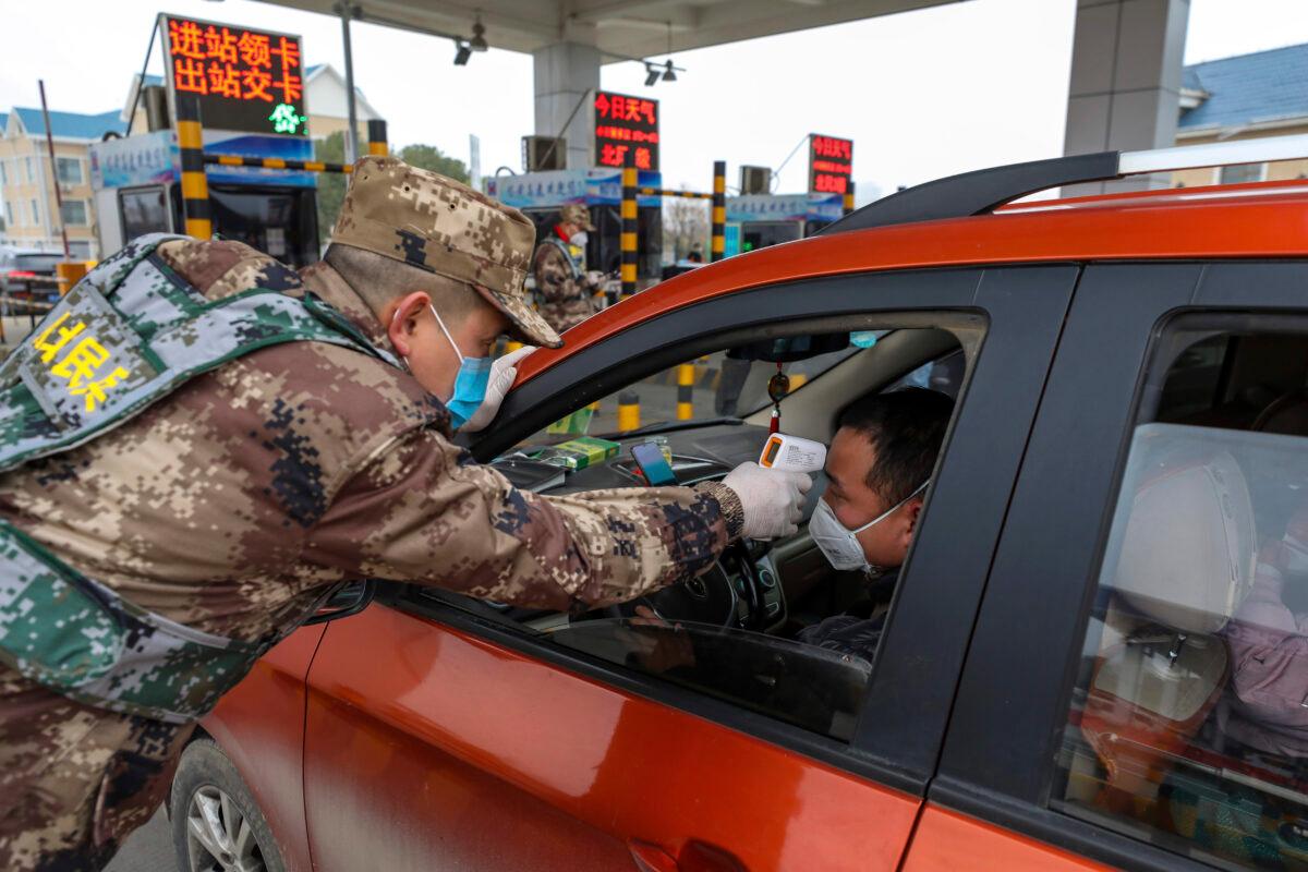 A militia member uses a digital thermometer to take a driver's temperature at a checkpoint at a highway toll gate in Wuhan in central China's Hubei Province on Jan. 23, 2020. (Chinatopix via AP)