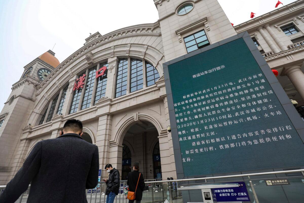 People walk past a billboard announcing the closure of the Hankou Railway Station in Wuhan in central China's Hubei Province on Jan. 23, 2020. (Chinatopix via AP)