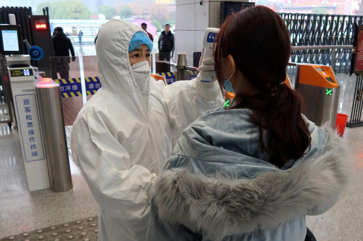 A worker in protective suits checks the temperature of a passenger arriving at the Xianning North Station on the eve of the Chinese Lunar New Year celebrations, in Xianning, a city bordering Wuhan to the north, in Hubei province, China on Jan. 24, 2020. (Martin Pollard/Reuters)
