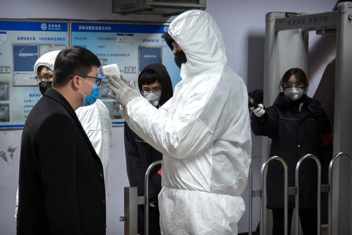 A worker wearing a hazardous materials suit takes the temperature of a passenger at the entrance to a subway station in Beijing on Jan. 26, 2020. (Mark Schiefelbein/AP Photo)