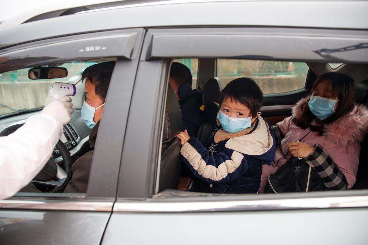 A medical worker in a protective suit checks the body temperature of a driver at a checkpoint outside the city of Yueyang, Hunan province, China, on Jan. 28, 2020. (Thomas Peter/Reuters)