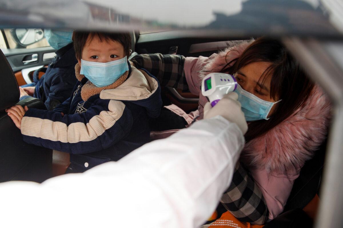 A medical worker in a protective suit checks the body temperature of a driver at a checkpoint outside the city of Yueyang, Hunan Province, near the border to Hubei Province that is on lockdown after an outbreak of a new coronavirus, in China on Jan. 28, 2020. (Thomas Peter/Reuters)