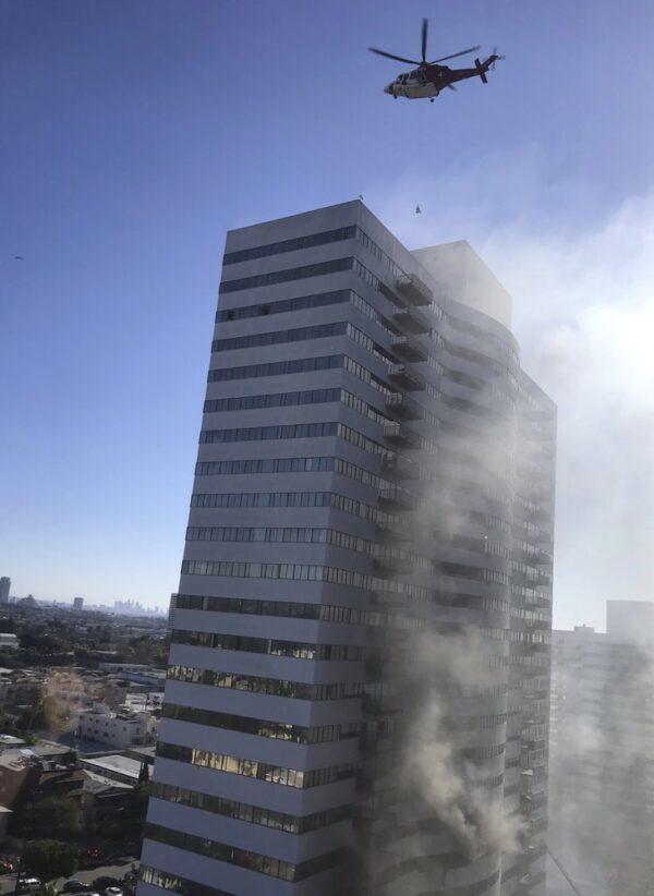 A helicopter flies over a residential building that is on fire in Los Angeles,  Calif., on Jan. 29, 2020. Firefighters swarmed the building on the city's west side and people could be seen on the roof as flames and smoke rise from the sixth floor. A helicopter was hoisting people off the roof. (Megan Feldman via AP)