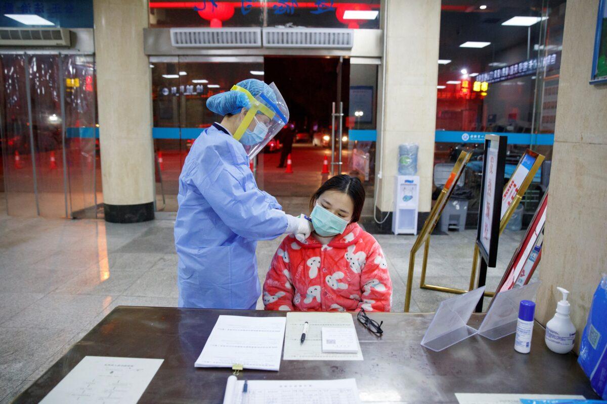 A nurse takes the temperature of a woman in the reception area of the First People's Hospital in Yueyang, Hunan Province, near the border to Hubei Province, which is under partial lockdown after an outbreak of a new coronavirus, in China on Jan. 28, 2020. (Thomas Peter/Reuters)