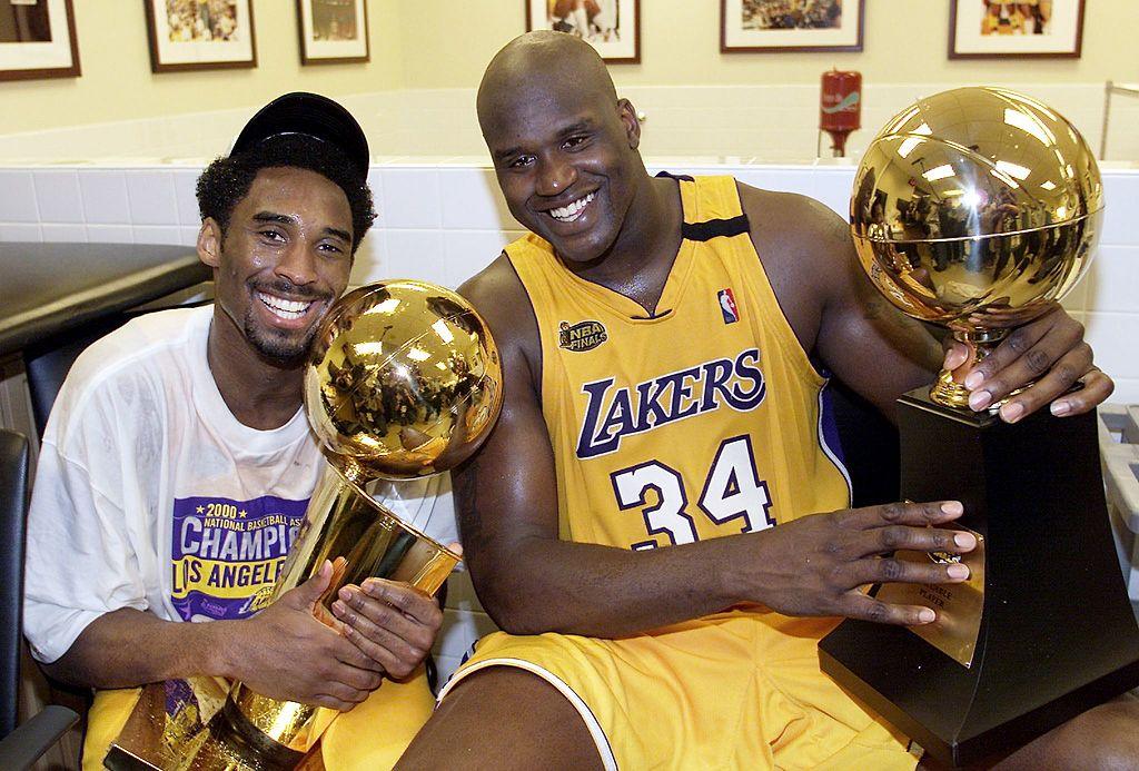 Bryant (L) holds the Larry O'Brian trophy as teammate O'Neal (R) holds the MVP trophy after winning the NBA Championship against Indiana Pacers on June 19, 2000. (©Getty Images | <a href="https://www.gettyimages.com/detail/news-photo/kobe-bryant-of-the-los-angeles-lakers-holds-the-larry-news-photo/51549493?adppopup=true">AFP</a>)
