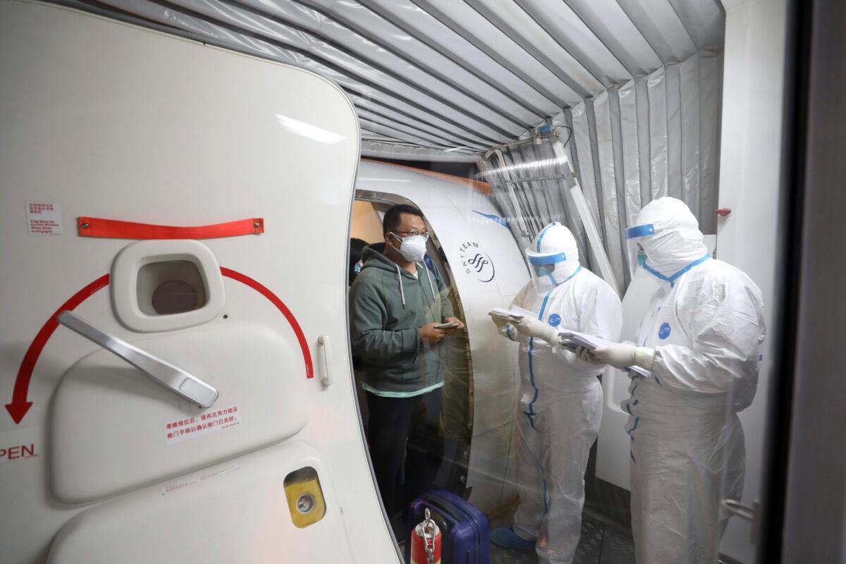 Quarantine workers in protective suits check identity documents as tourists from the Wuhan area walk off of a chartered plane taking them home from Bangkok at Wuhan Tianhe International Airport in Wuhan in central China's Hubei Province on Jan. 31, 2020. (Chinatopix via AP)