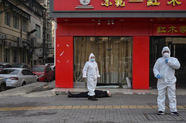 Chinese officials in protective suits checking on an elderly man wearing a facemask who collapsed and died on a street near a hospital in Wuhan, China, on Jan. 30, 2020. (HECTOR RETAMAL/AFP via Getty Images)