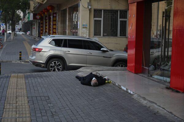 An elderly man wearing a facemask lies on the pavement after he collapsed and died along a street near a hospital in Wuhan on Jan. 30, 2020. (HECTOR RETAMAL/AFP via Getty Images)