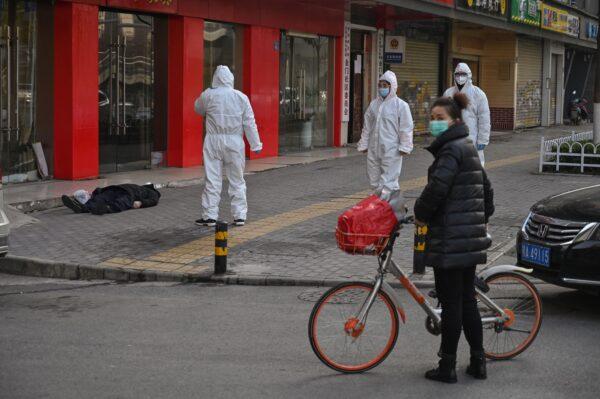 Chinese officials in protective suits checking on an elderly man wearing a facemask who collapsed and died on a street near a hospital in Wuhan, China, on Jan. 30, 2020. AFP journalists saw the body not long before an emergency vehicle arrived carrying police and medical staff in full-body protective suits. (HECTOR RETAMAL/AFP via Getty Images)