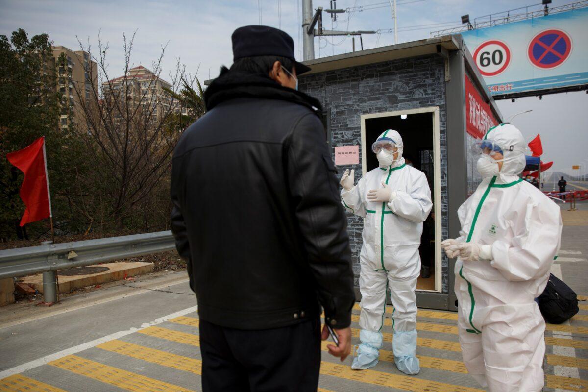 Hospital staff in protective clothing talk to a police officer at a checkpoint to the Hubei province exclusion zone at the Jiujiang Yangtze River Bridge in Jiujiang, Jiangxi province, China, as the country is hit by an outbreak of a new coronavirus on Feb. 1, 2020. (Thomas Peter/Reuters)