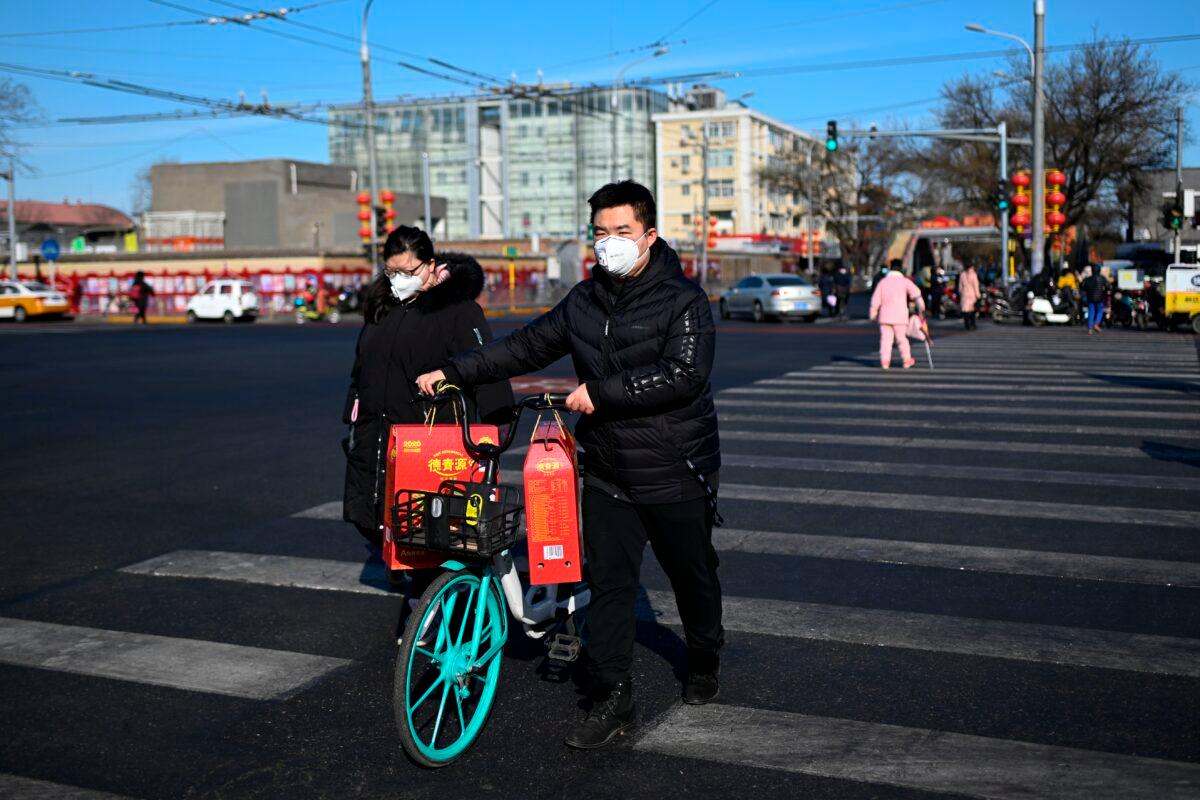 A man, wearing a mask, pushes a sharing bicycle with goods crossing a street in Beijing on Feb. 1, 2020. (Wang Zhao/AFP via Getty Images)