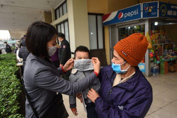 An employee (L) puts a protective face mask on a child at a railway station in Hanoi, Vietnam, on Feb. 2, 2020. (Nhac Nguyen/AFP via Getty Images)