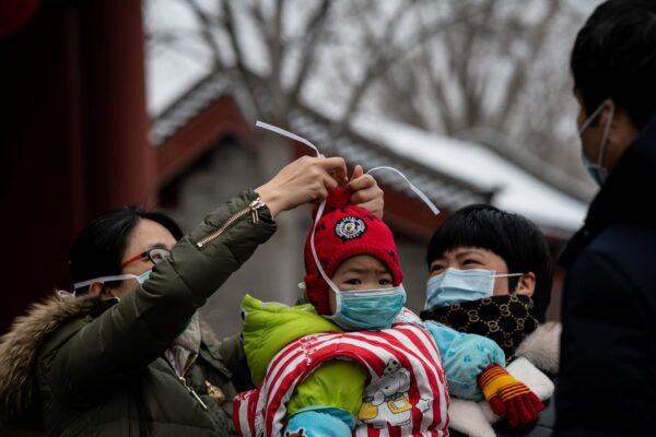 A woman (L) puts a protective mask to prevent the spread of the SARS-like virus on a child at the Jingshan park in Beijing on Feb. 2, 2020. (NICOLAS ASFOURI/AFP via Getty Images)