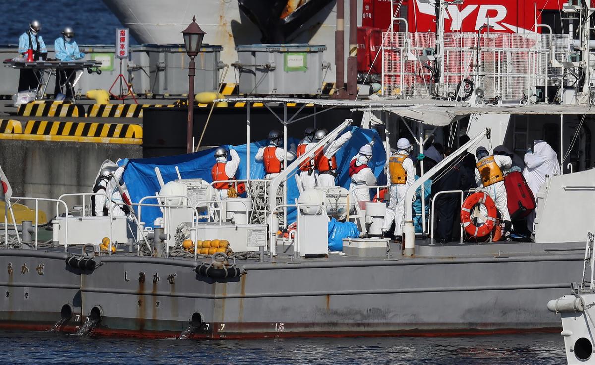 Workers in protective gear transfer a person under a blue sheet from the Diamond Princess cruise ship onto a Japan Coast Guard boat in Yokohama on Feb. 5, 2020. (STR/JIJI PRESS/AFP via Getty Images)
