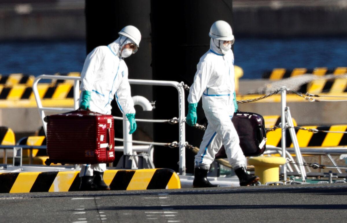 Officers in protective gears carry luggage cases after people who were transferred from cruise ship Diamond Princess arrive at a maritime police's base in Yokohama, south of Tokyo on Feb. 5, 2020. (Kim Kyung-Hoon/Reuters)
