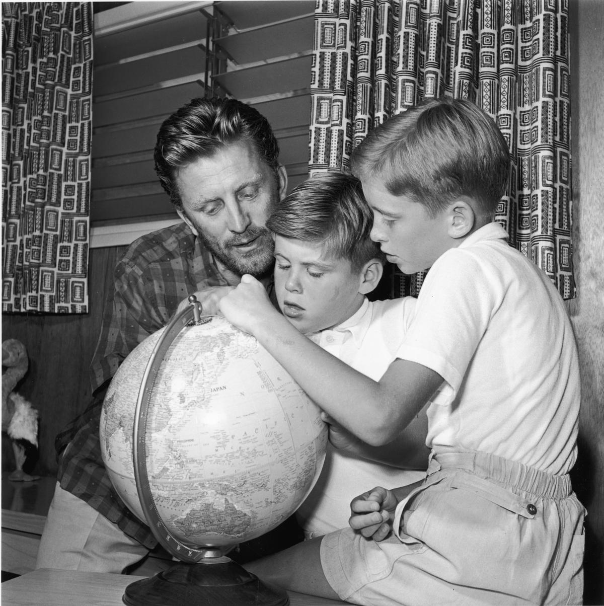 Douglas inspects a globe with two of his sons, Joel (L) and Michael (R), circa 1956 (©Getty Images | <a href="https://www.gettyimages.com/detail/news-photo/american-actor-kirk-douglas-looks-at-a-world-globe-with-two-news-photo/1858205">Arnold M. Johnson/Hulton Archive</a>)