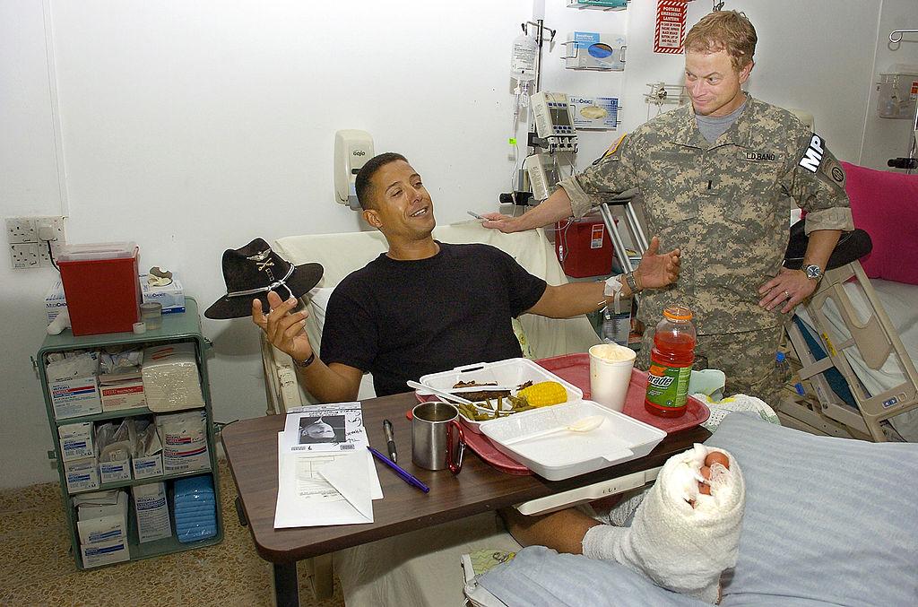 Gary Sinise listens to US Army CW 4 Leif Neely of Woodbridge, Virginia, tell about how he was wounded while flying his Kiowa Warrior helicopter on a mission over Mosul, Iraq, on May 20, 2007. (©Getty Images | <a href="https://www.gettyimages.com/detail/news-photo/in-this-handout-provided-by-the-uso-actor-gary-sinise-news-photo/74210354?adppopup=true">Mike Theiler/USO</a>)