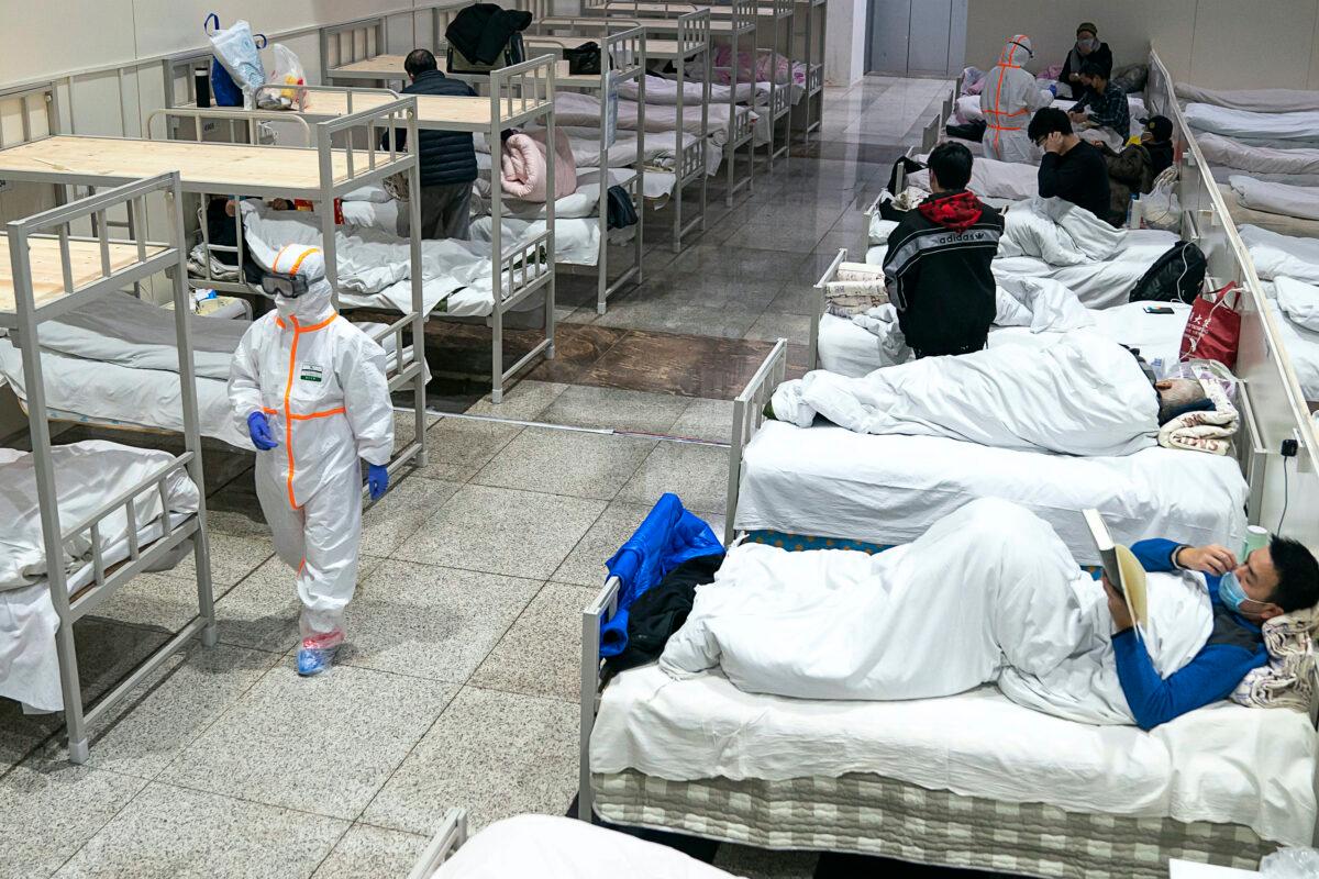 A medical worker in a protective suit walks by patients diagnosed with the coronavirus in a temporary hospital transformed from an exhibition center in Wuhan in central China's Hubei Province on Feb. 5, 2020. (Chinatopix via AP)
