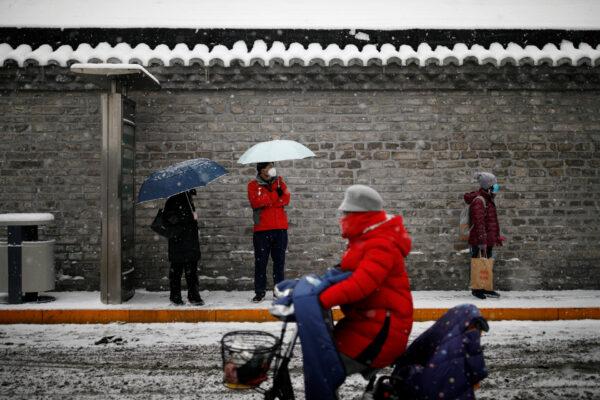 People wearing masks wait amid snow at a bus stop as the country is hit by an outbreak of the novel coronavirus, in Beijing, China, on Feb. 6, 2020. (Carlos Garcia Rawlins/Reuters)