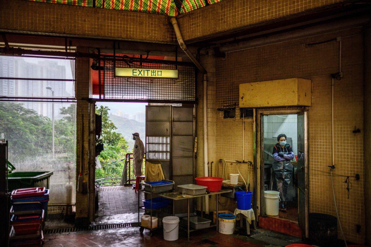 A police officer (L) wears protective gear as he guards a cordon near a public toilet as a member of staff (R) stands in the doorway of a restaurant kitchen outside Hong Mei House at the Cheung Hong Estate in Hong Kong on Feb. 11, 2020, following the evacuation of more than 100 people from the housing block after four residents in two different apartments tested positive for COVID-19. (Anthony Wallace/AFP via Getty Images)