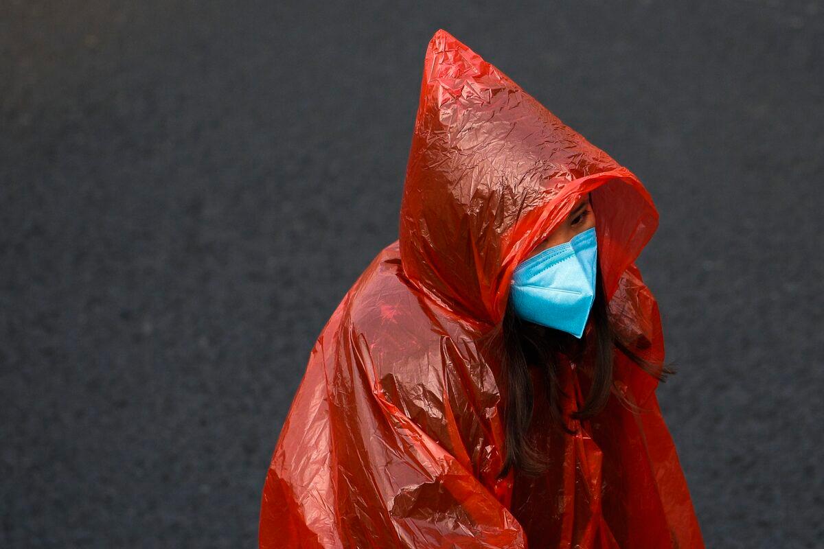 A masked woman in a plastic rain coat walks on a street in Beijing on Feb. 11, 2020. (Andy Wong/AP Photo)