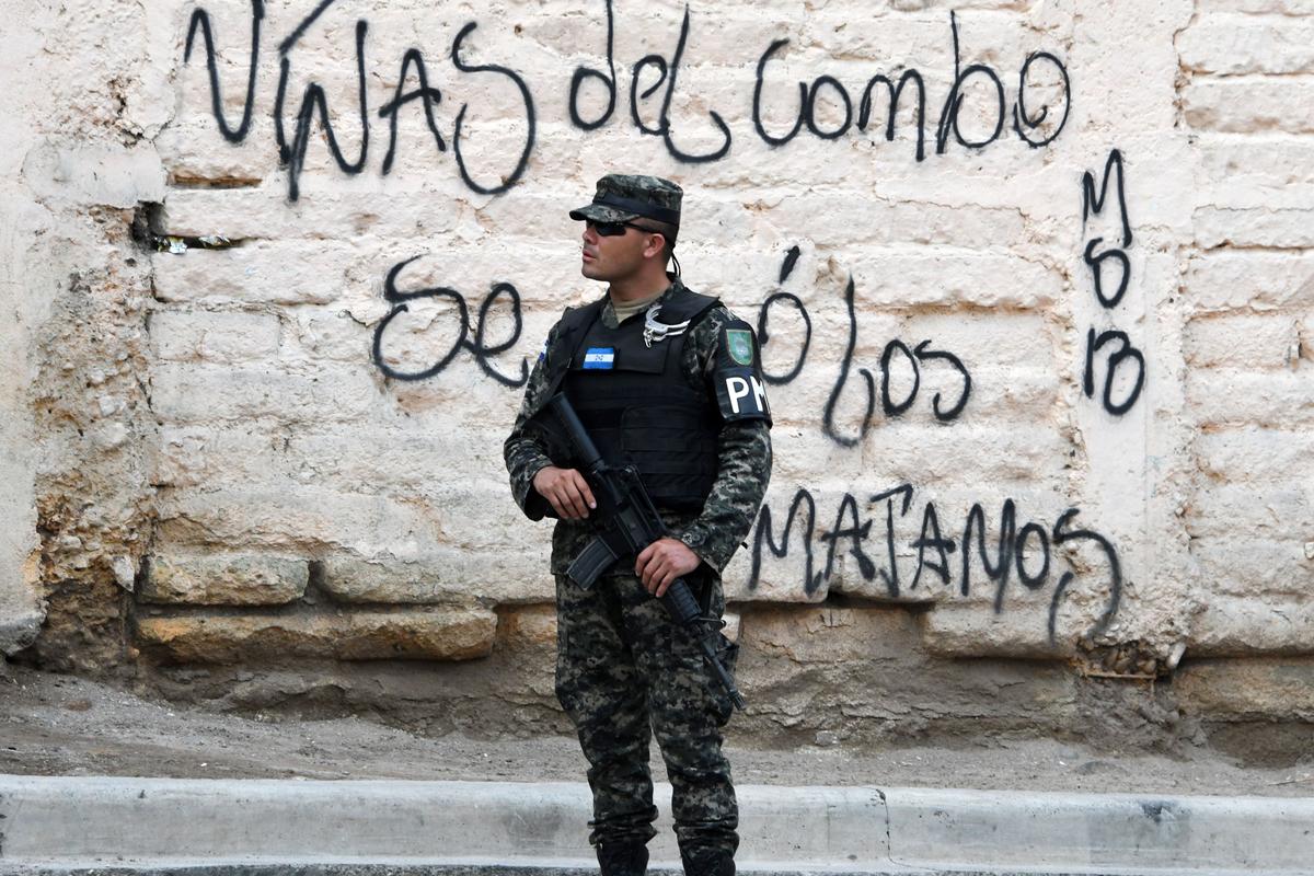 A Military Police soldier stands by a graffiti made by the Mara Salvatrucha (MS-13) gang that reads "Girls Of The Combo Go Away Or We'll Kill You," in the MS-13-controlled El Bosque neighborhood in Tegucigalpa, Honduras, on May 9, 2017. (Orlando Sierra/AFP via Getty Images)