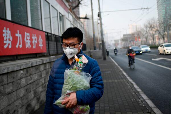 A man wearing a face mask and holding a bag of vegetables walks along a street in Beijing on Feb. 12, 2020. (STR/AFP via Getty Images)