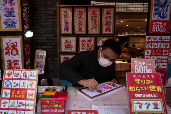 In this Feb. 13, 2020, photo, a vendor wears a mask while writing calligraphy for customers in Yokohama's Chinatown, near Tokyo. (Jae C. Hong/AP Photo)