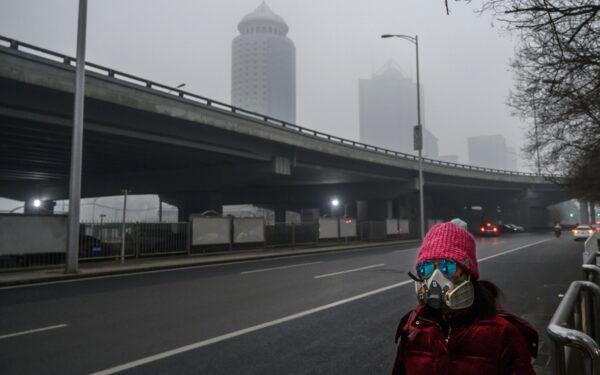 A Chinese woman waits for a bus on a nearly empty road during rush hour in the central business district in Beijing on Feb. 13, 2020. (Kevin Frayer/Getty Images)