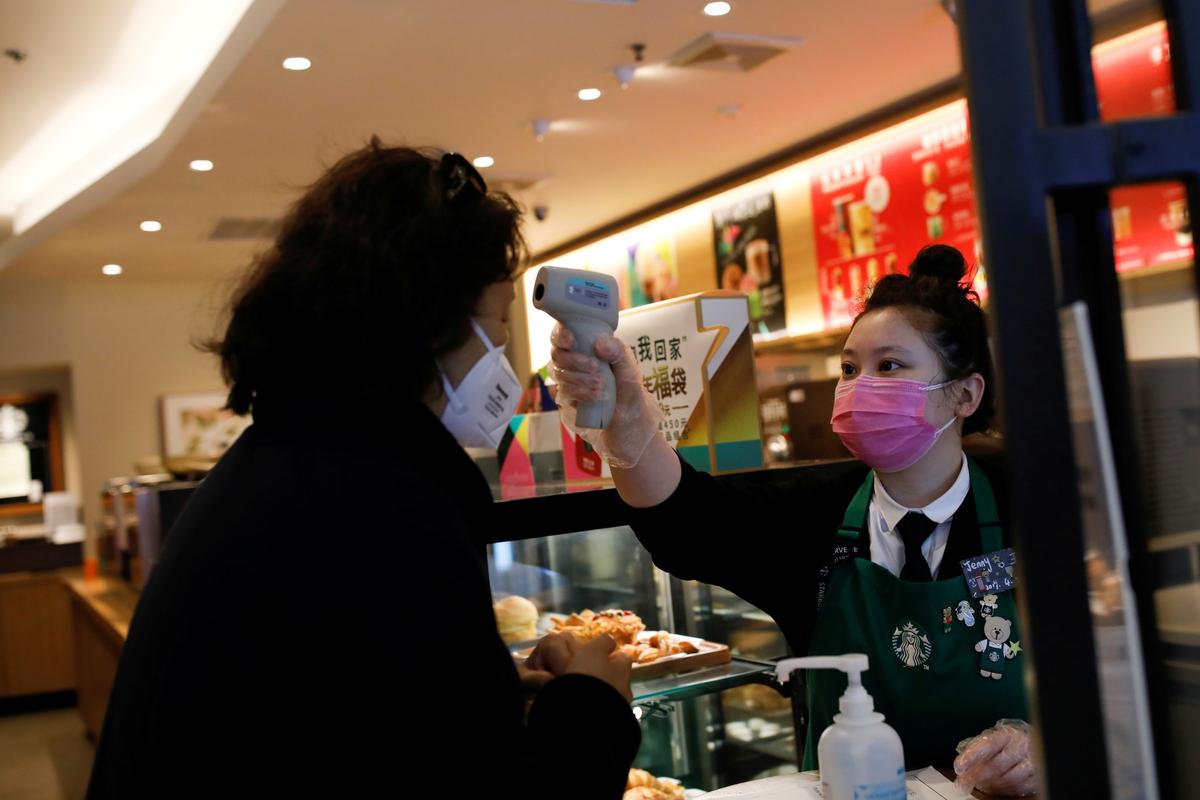 A worker uses a thermometer to check the temperature of a customer as she enters a Starbucks shop as the country is hit by an outbreak of the new coronavirus, in Beijing, China on Jan. 30, 2020. (Carlos Garcia Rawlins/Reuters)