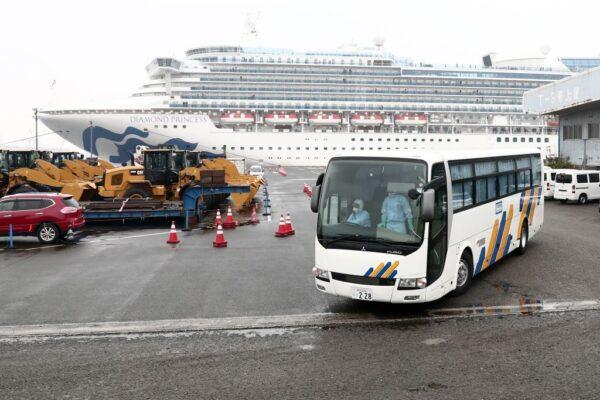 A bus with a driver (L) wearing protective gear departs from the dockside next to the Diamond Princess cruise ship, at the Daikoku Pier Cruise Terminal in Yokohama port in Japan on Feb. 16, 2020. (Behrouz Mehri/AFP via Getty Images)