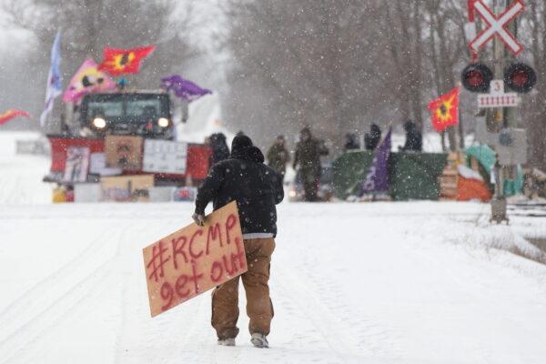 A protester carries a sign at a rail blockade on in Tyendinaga, near Belleville, Ont., on Feb. 15, 2020. (The Canadian Press/Lars Hagberg)