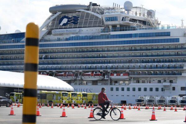 A man cycles past city buses (back L) lined up to transport the first batch of passengers disembarking from the Diamond Princess cruise ship at the Daikoku Pier Cruise Terminal in Yokohama on Feb. 19, 2020. (Charly Triballeau/AFP via Getty Images)