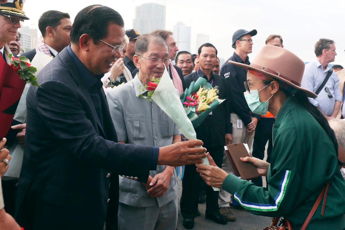 In this Feb. 14, 2020, file photo, Cambodia's Prime Minister Hun Sen, left, gives a bouquet of flowers to a passenger who disembarked from the MS Westerdam at the port of Sihanoukville, Cambodia. (Heng Sinith/AP Photo)